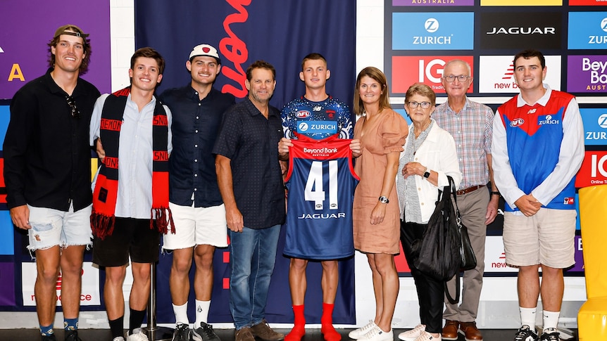 Football club rooms, with a player holding up guernsey surrounded by family.