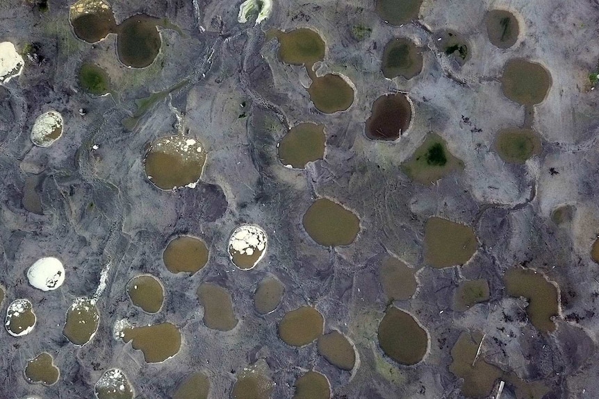 An aerial photo shows water-filled holes blasted in the sandy landscape.
