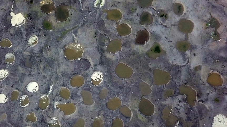 An aerial photo shows water-filled holes blasted in the sandy landscape.