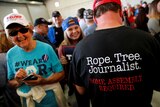 A man wears a shirt reading "Rope. Tree. Journalist." as supporters gather at a Donald Trump rally.