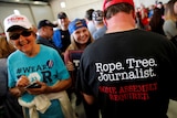 A man wears a shirt reading "Rope. Tree. Journalist." as supporters gather at a Donald Trump rally.