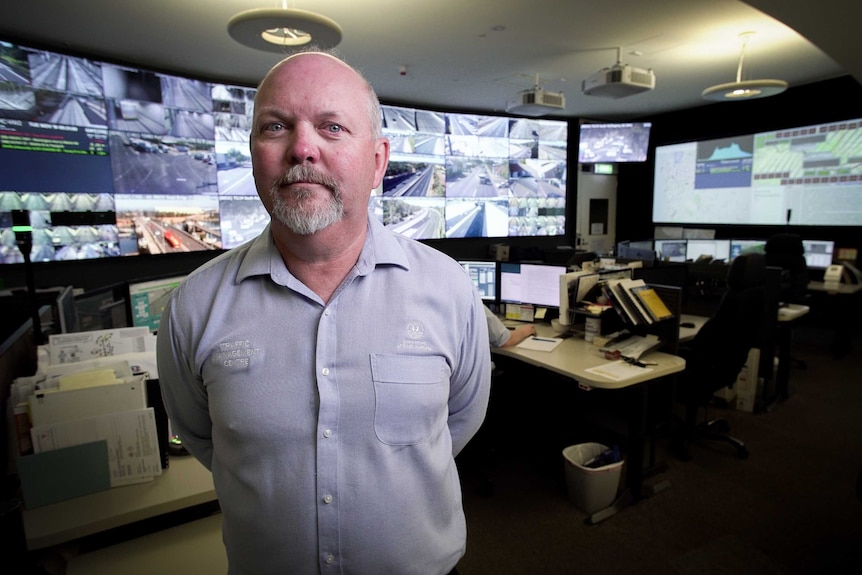 A man in front of a wall of screens with roads on them