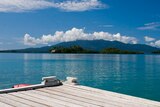 Looking from a wooden jetty, you few tranquil turquoise waters with a mountain sitting on the horizon line.