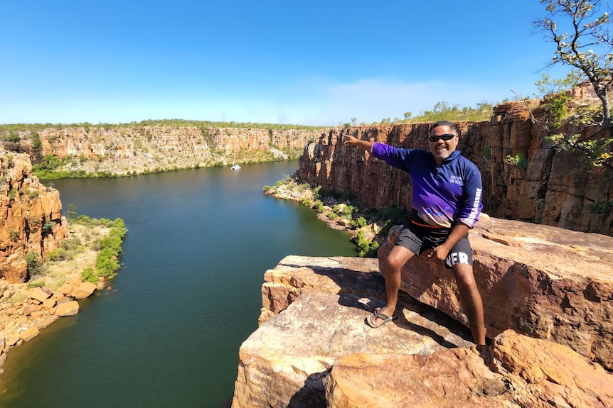 A man, smiling, points to waterfalls.