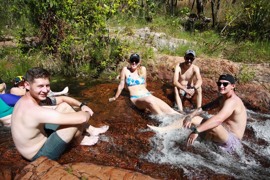 Four happy people are sitting in a rock hole and smile at the camera.