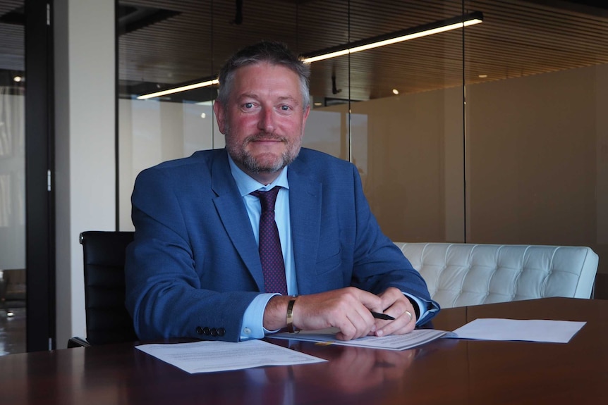 A man in a suit sits at a desk.