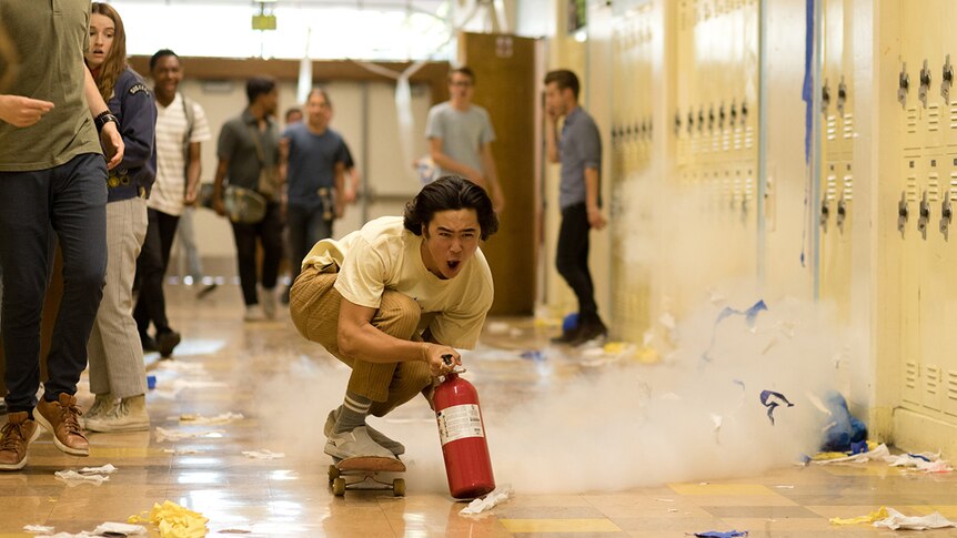 Colour film still of Nico Hiraga skateboarding down school hallway with fire extinguisher in 2019 film Booksmart.