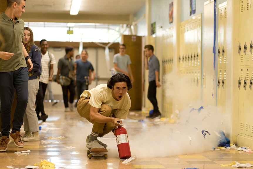 Colour film still of Nico Hiraga skateboarding down school hallway with fire extinguisher in 2019 film Booksmart.