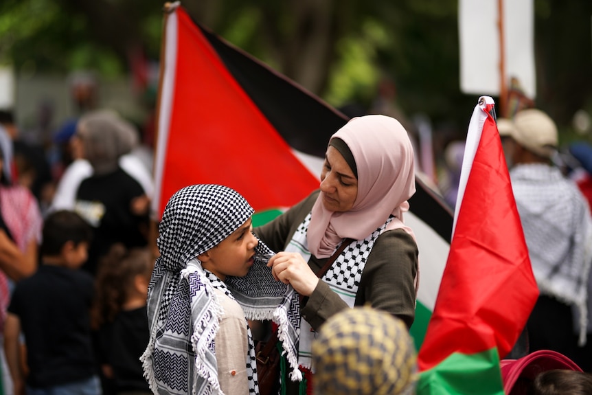 A woman wraps a palestinian scarf around a young boy at a rally in sydney's Hyde Park