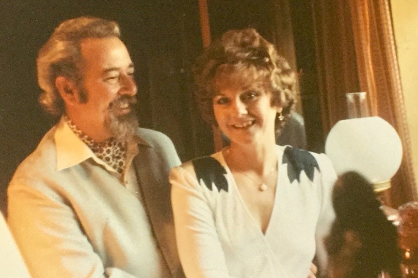A man and woman in 80s attire smiling together towards the camera