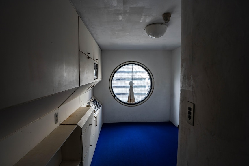 一间很小的空房间，有圆窗、蓝色地毯和墙上的传统电话