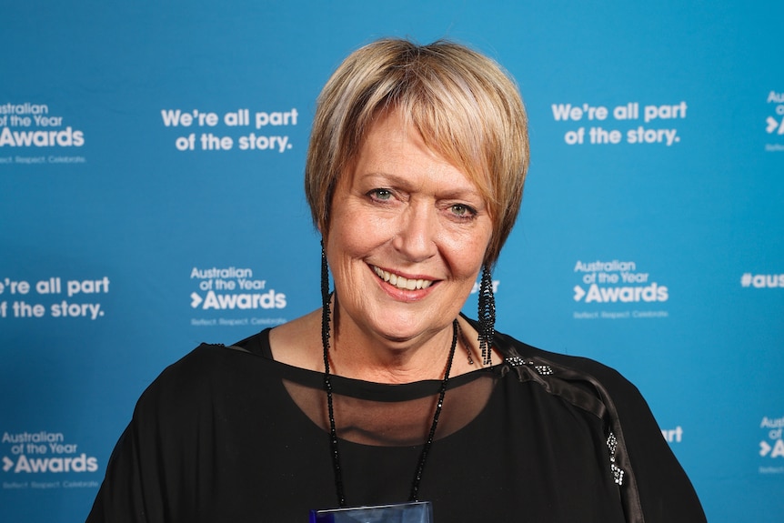 A woman smiles in front of a blue background.