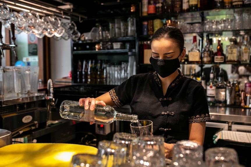 A woman holds a glass bottle filled with liquid in her hand, and pours it into a glass.