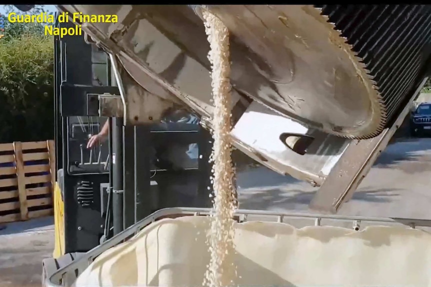 Thousands of pills are poured out of a heavy metal container into a huge bucket.