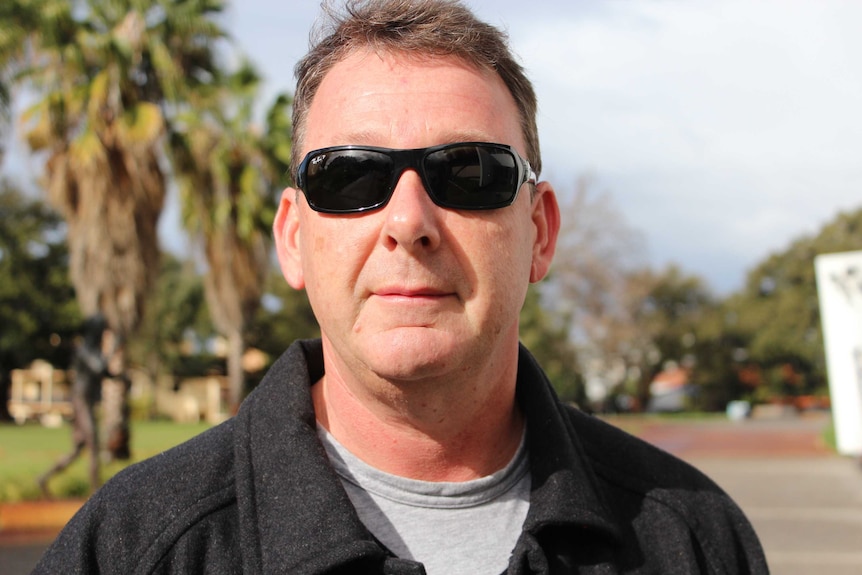 Close up of a man wearing sunglasses, with palm trees in background.