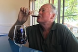 Winemaker Terry Mulligan sampling a glass of cherry wine with a glass of cherries in front of him.