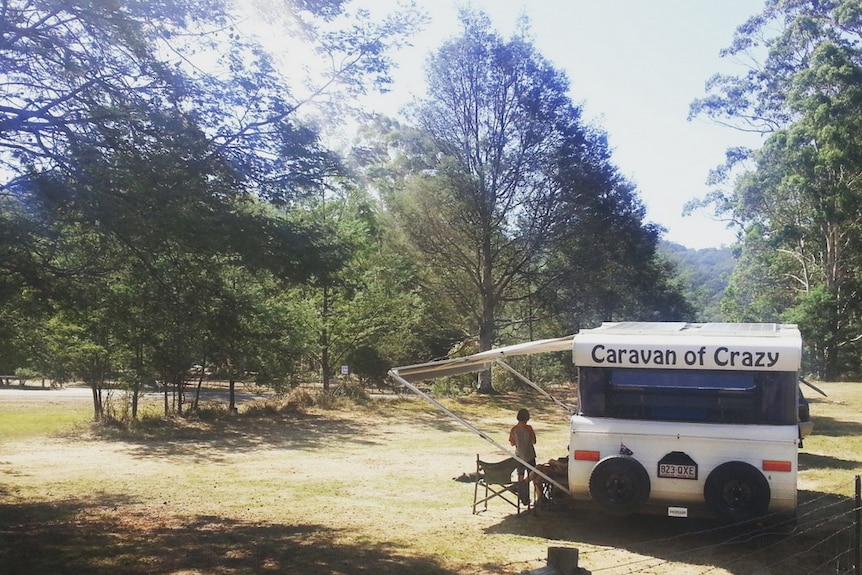 A van dubbed the 'Caravan of Crazy' parks on the side of a wooded road.