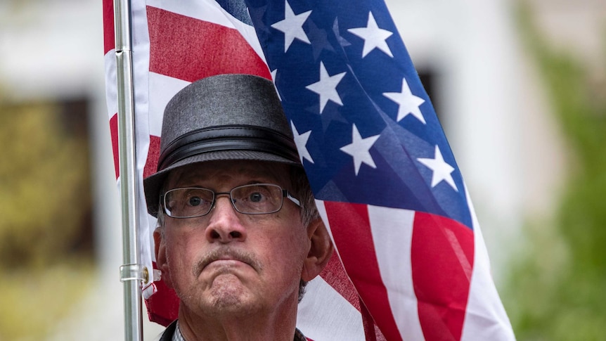 A man in a hat wrapped in an American flag makes an exaggerated pout