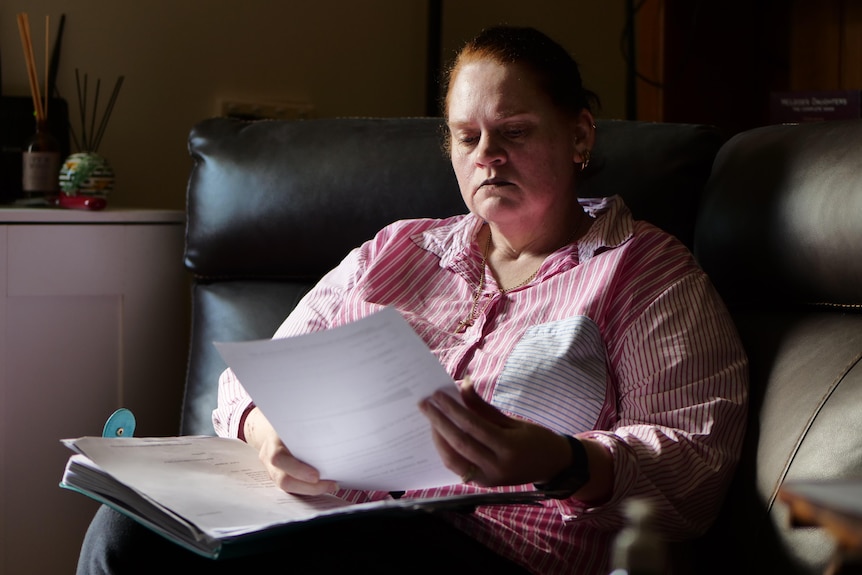 A woman sits on a lounge chair looking at a piece of paper as the sun shines through a window on to her face