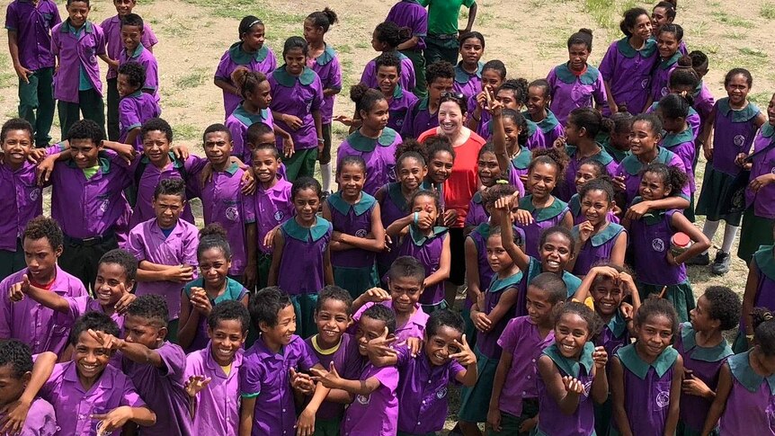 Rebecca McDonald wears a red shirt, surrounded by school children in purple uniforms.