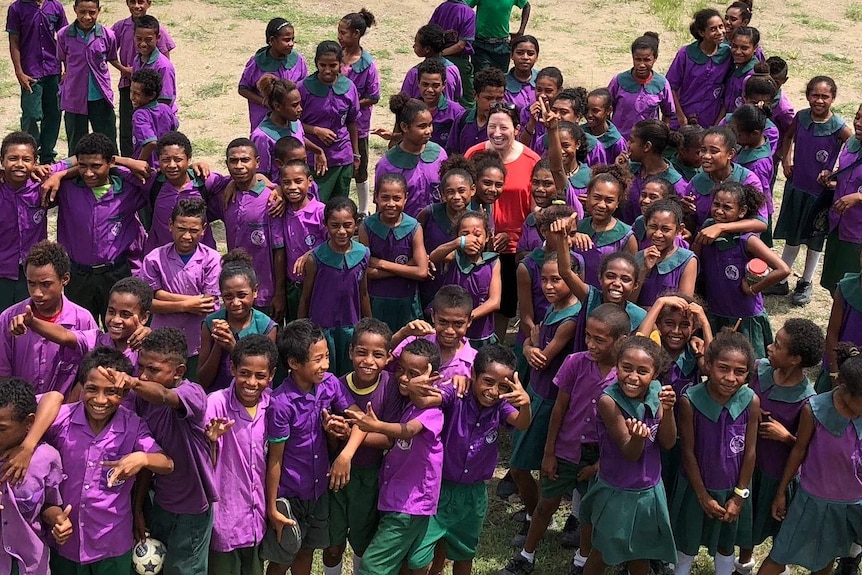 Rebecca McDonald wears a red shirt, surrounded by school children in purple uniforms.