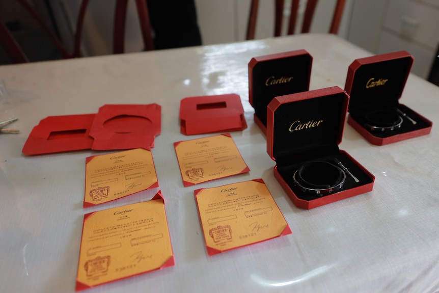 Three open boxes with Cartier logo and silver bracelets inside, paperwork next to it