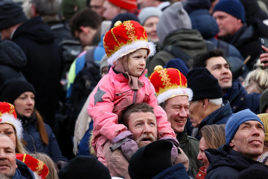 A child in a fake crown sits on a man's shoulders
