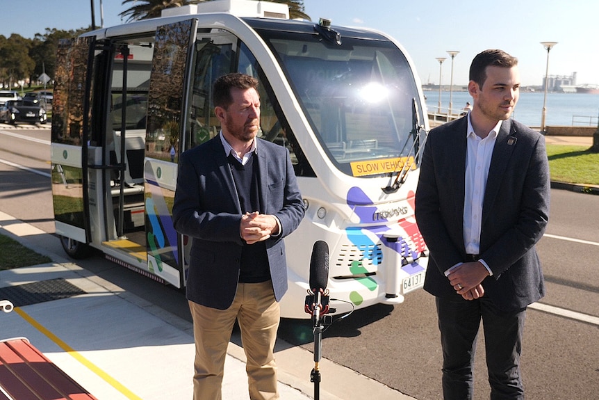 Two  men and a very small bus at a press conference.