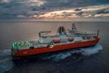 Ship at sea in dawn light, with helicopter pad light up on deck