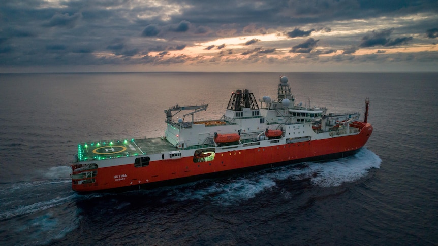 Ship at sea in dawn light, with helicopter pad light up on deck