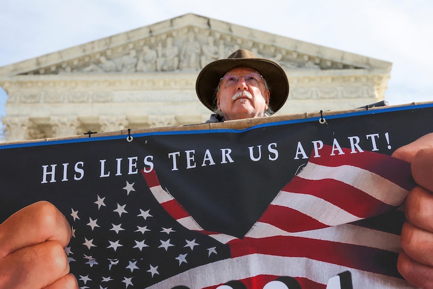 A protestor holds up a sign that says 'his lies tear us apart' outside court