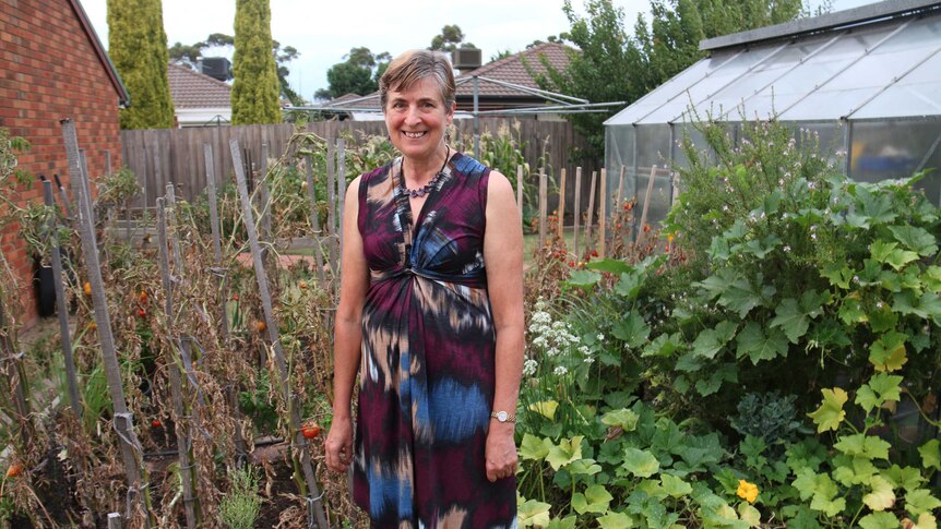 A woman stands in front of a backyard vegetable patch.