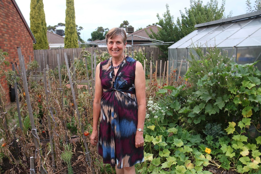 A woman stands in front of a backyard vegetable patch.