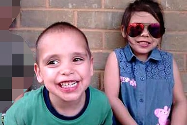 Three young children standing next a wall, their faces pixelated.