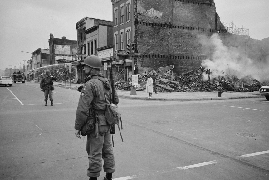 A black and white photo of National Guard soldiers on a damaged street corner
