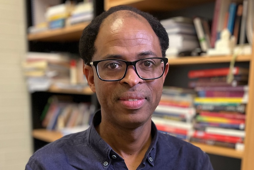 A man with glasses sitting in front of a bookcase full of books