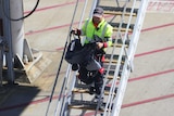 A man carries a pram down steps on the tarmac of an airport.