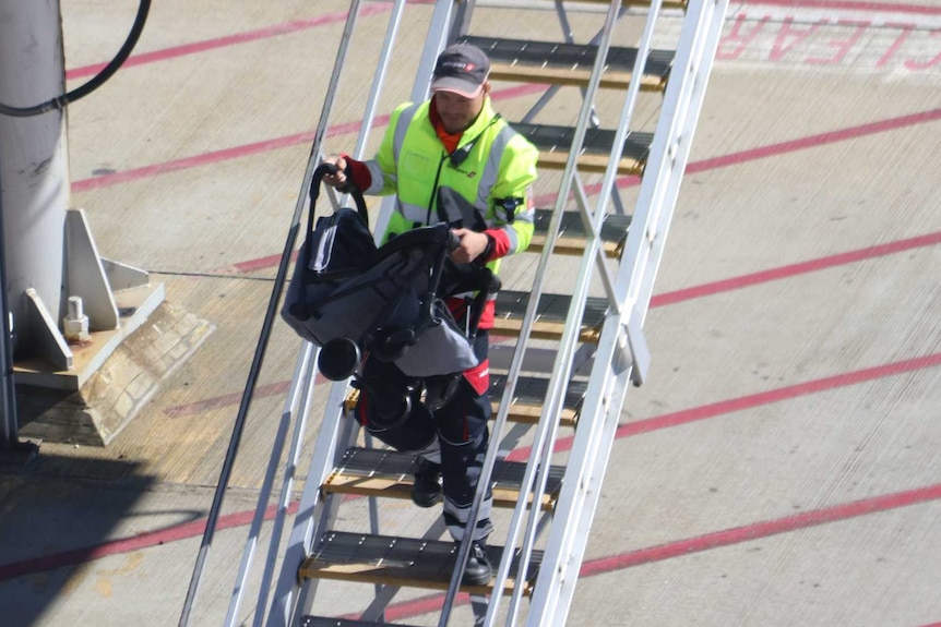 A man carries a pram down steps on the tarmac of an airport.