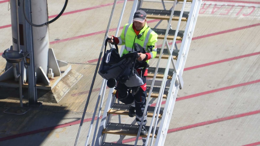 A man carries a pram down steps on the tarmac of an airport.