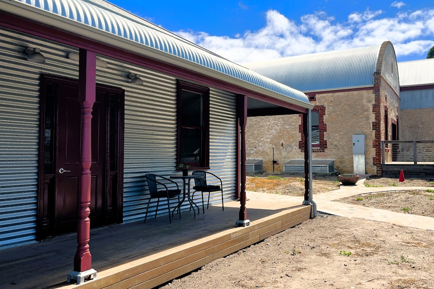A restored corrugated iron cottage with bull nose verandah sits alongside a stone building