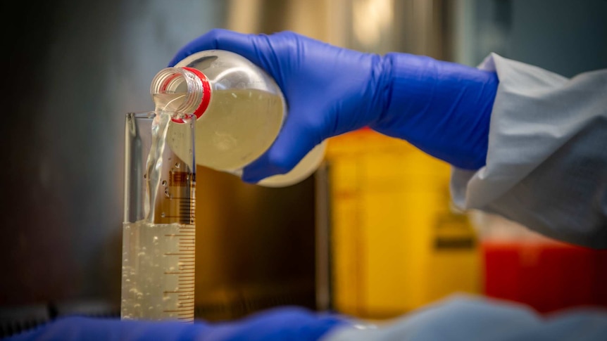 A hand pouring wastewater into a beaker