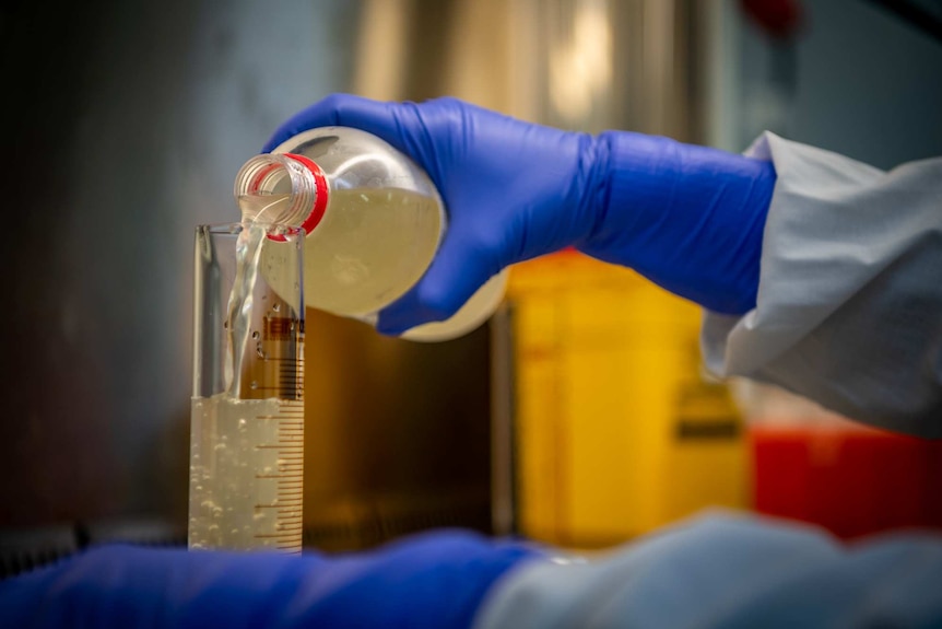 A hand pouring wastewater into a beaker