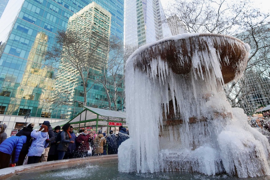 People pose for photographs in front of a frozen water fountain