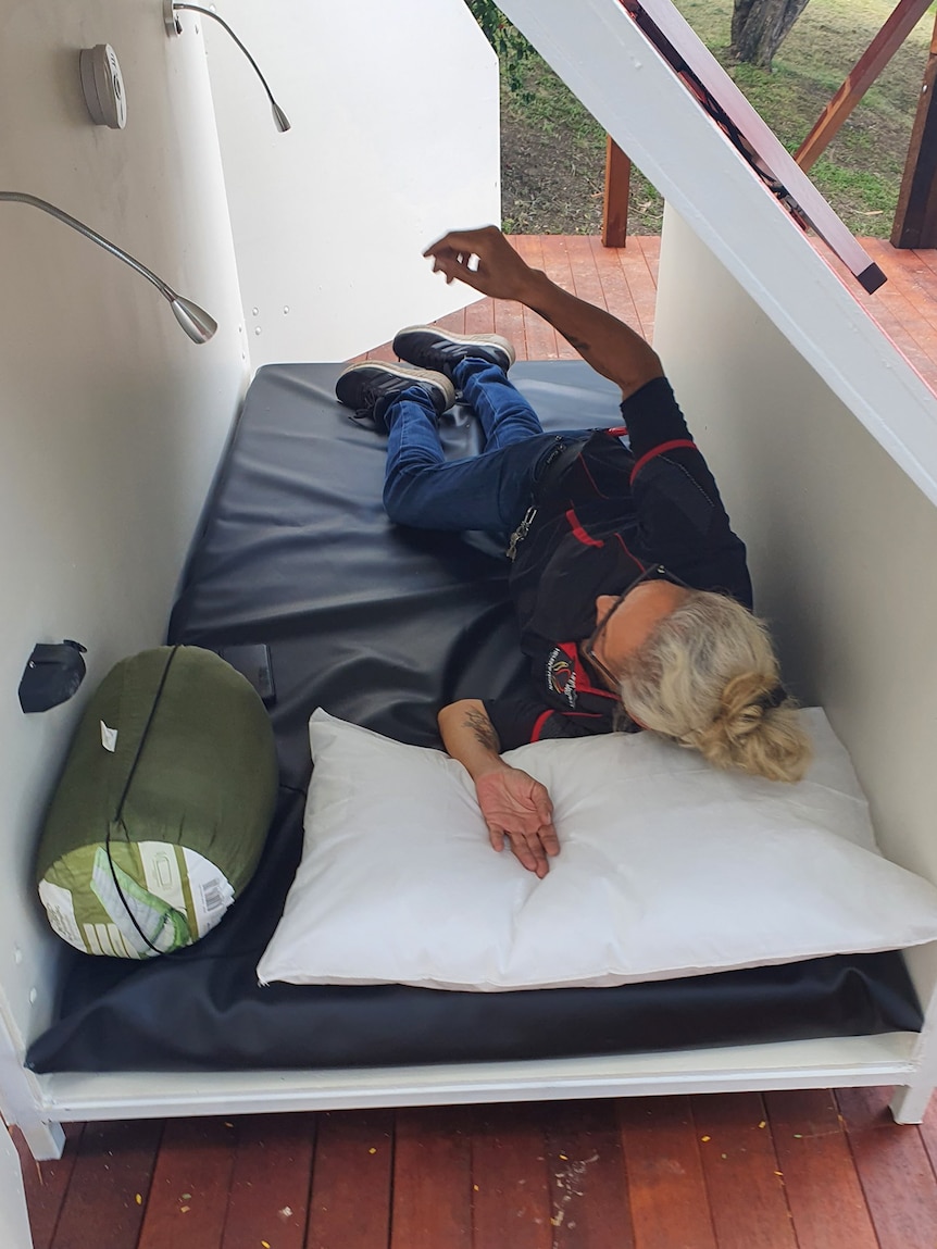 Lady laying on a bed inside a small pod with a sleeping bag.