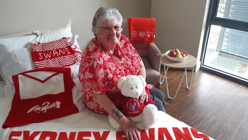 An elderly lady poses for a photo surrounded by Sydney Swans merchandise