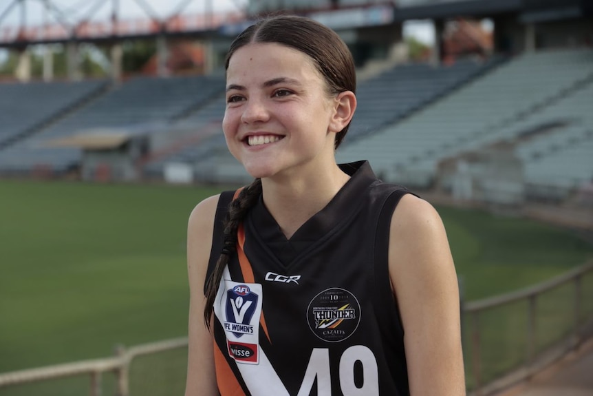 Emma, a smiling young woman looks off to the left of the picture. She's wearing a black football jersey.