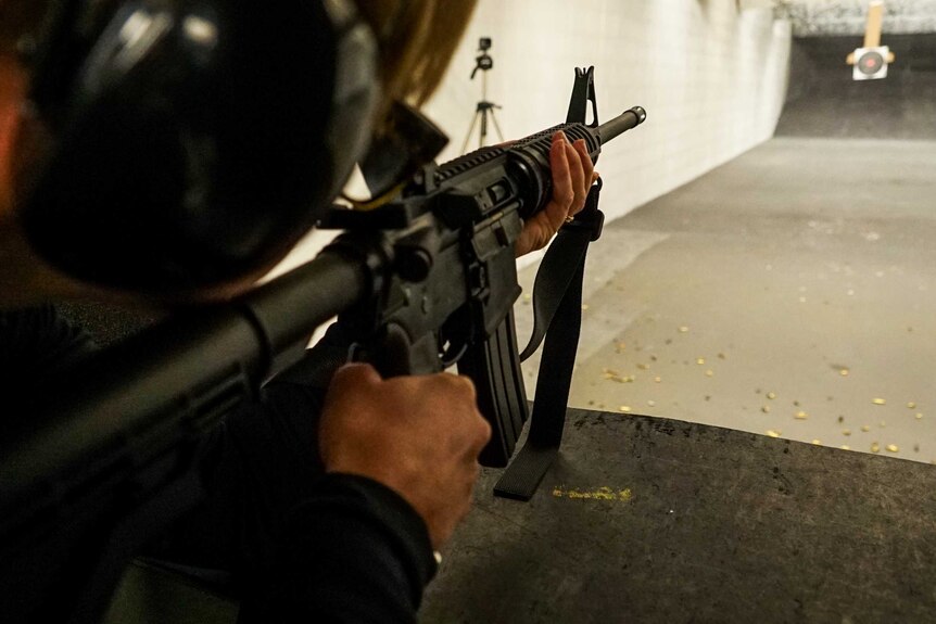 Close up of a shooter firing an AR15 at a rifle range, looking towards the target