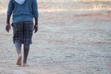 An anonymous young Indigenous boy walks alone outside in bare feet.