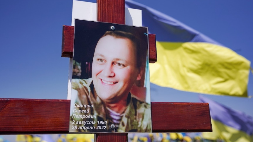 A picture of a smiling man's face, attached to a wooden cross outside.