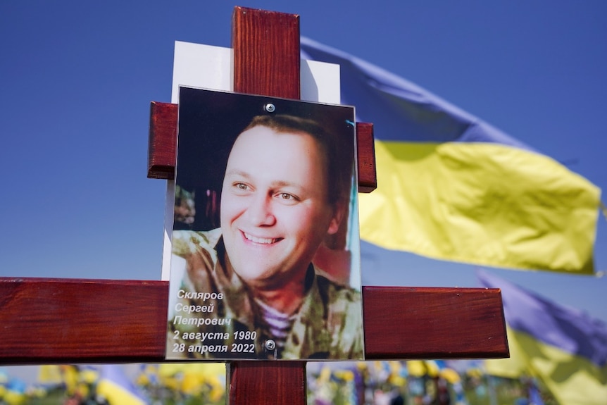 A picture of a smiling man's face, attached to a wooden cross outside.